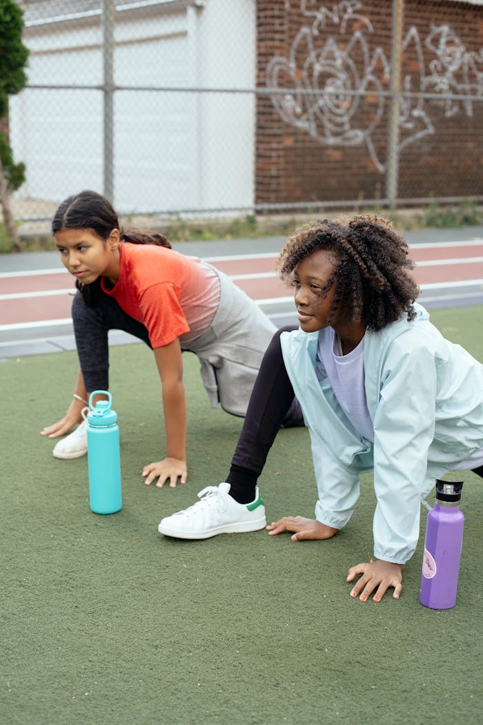 Two teenagers in sportswear stretching on an outdoor track, showcasing focus and concentration.